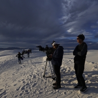 a film stands on sand dunes with camera equipment 